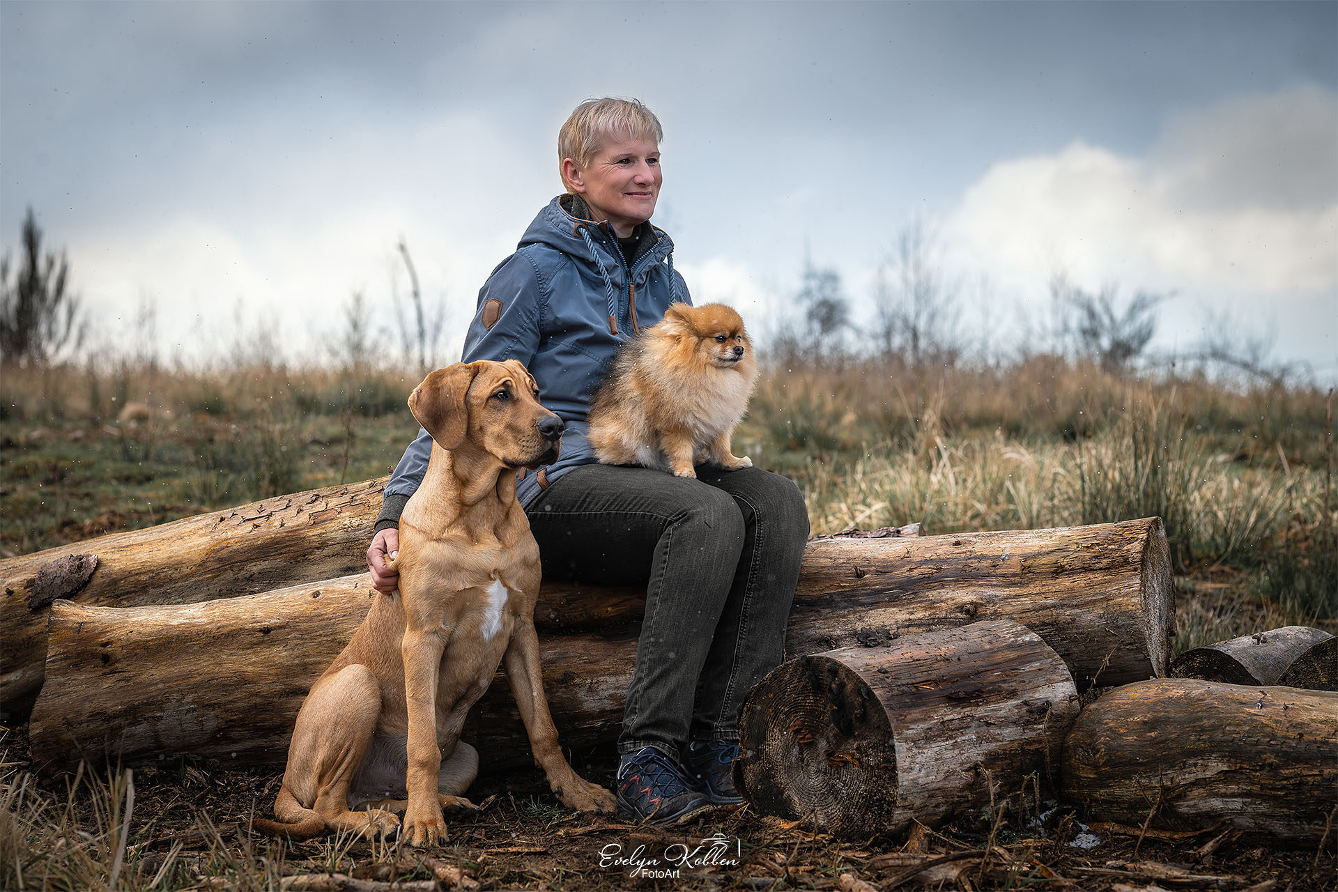 Eine naturverbundene junge Frau mit Ihrem Broholmer Junghund und Zwergspitz in der Landschaft
